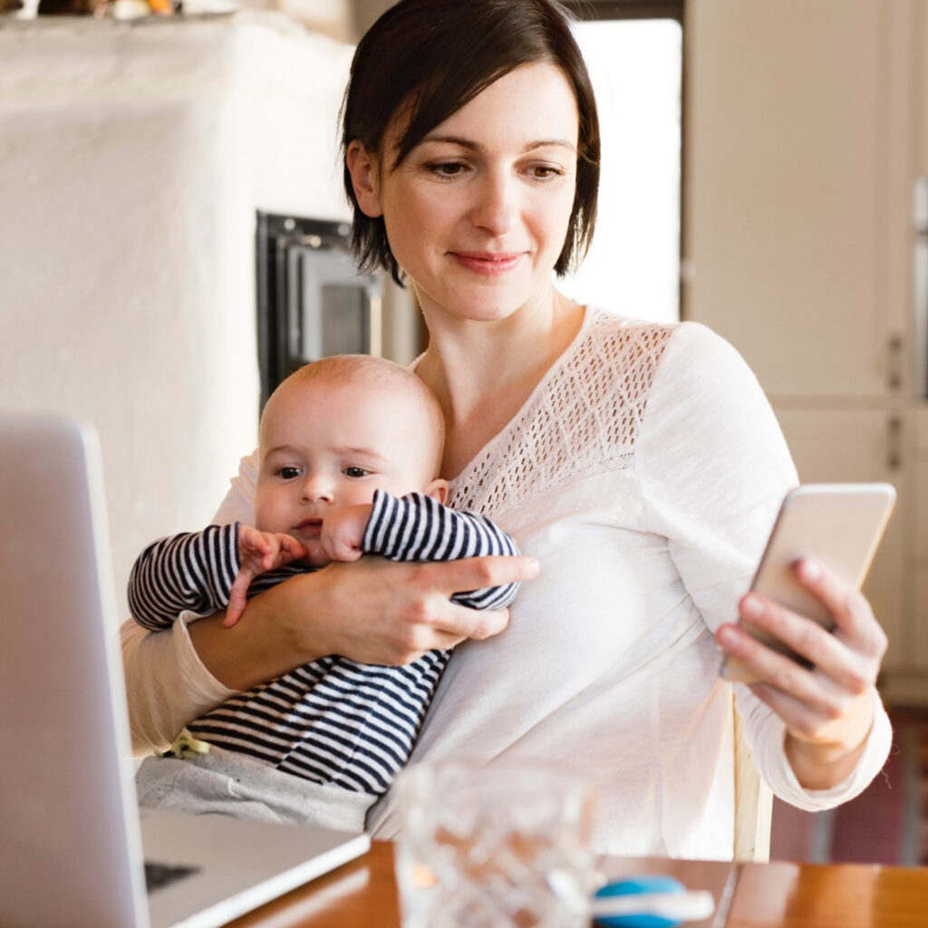 Woman holding a baby and viewing the app on their phone.